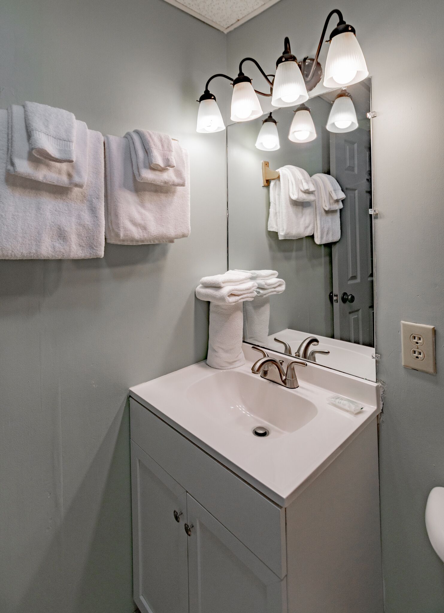 A bathroom with a white sink, a mirror, and multiple towels hanging on the wall.