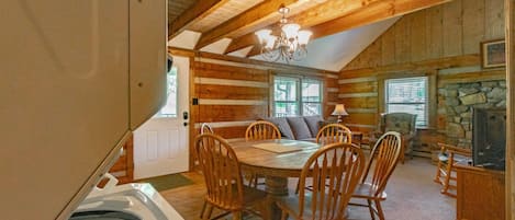 A cozy log cabin interior with a dining area, stone fireplace, and a large window.