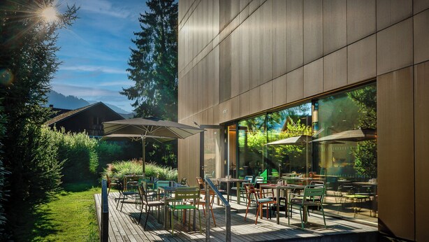 An outdoor patio with tables and chairs, a wooden deck, and a modern building with large windows.