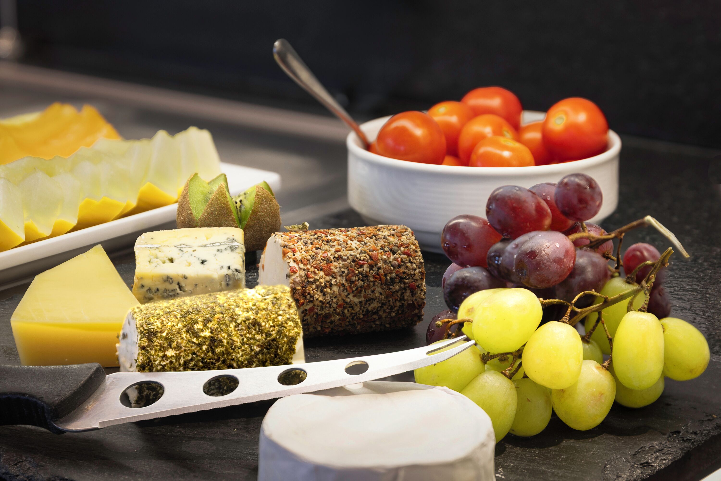 A variety of cheeses and grapes on a slate board.