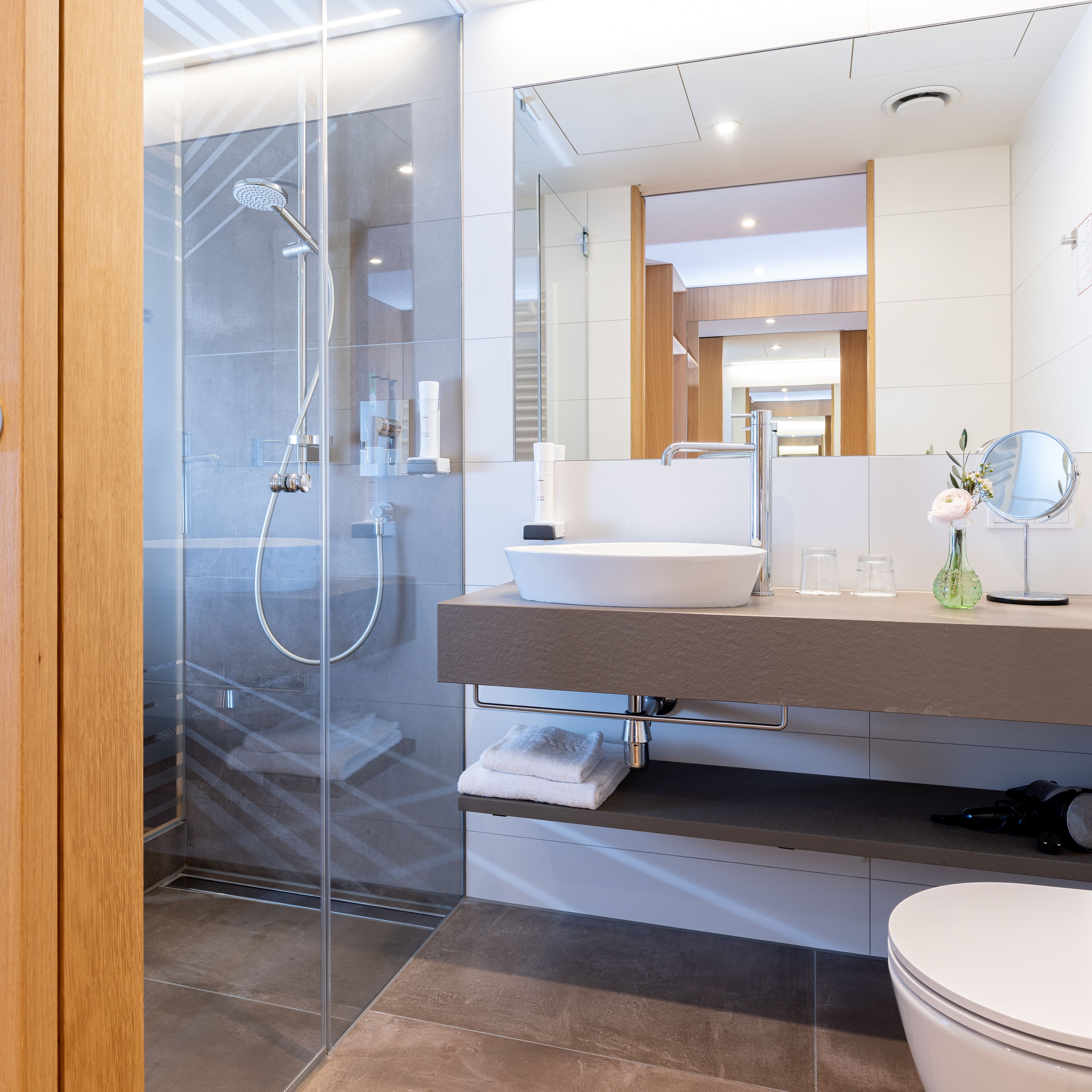 A modern bathroom with a glass-enclosed shower, a large mirror, and a white sink.
