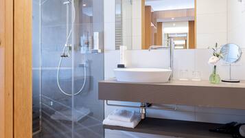A modern bathroom with a glass-enclosed shower, a large mirror, and a white sink.