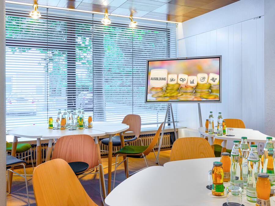 A modern conference room with round tables, chairs, and a large screen displaying a presentation.