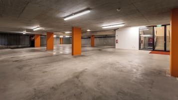 An indoor parking garage with concrete floors and orange pillars, featuring a fire extinguisher and emergency exit signs.