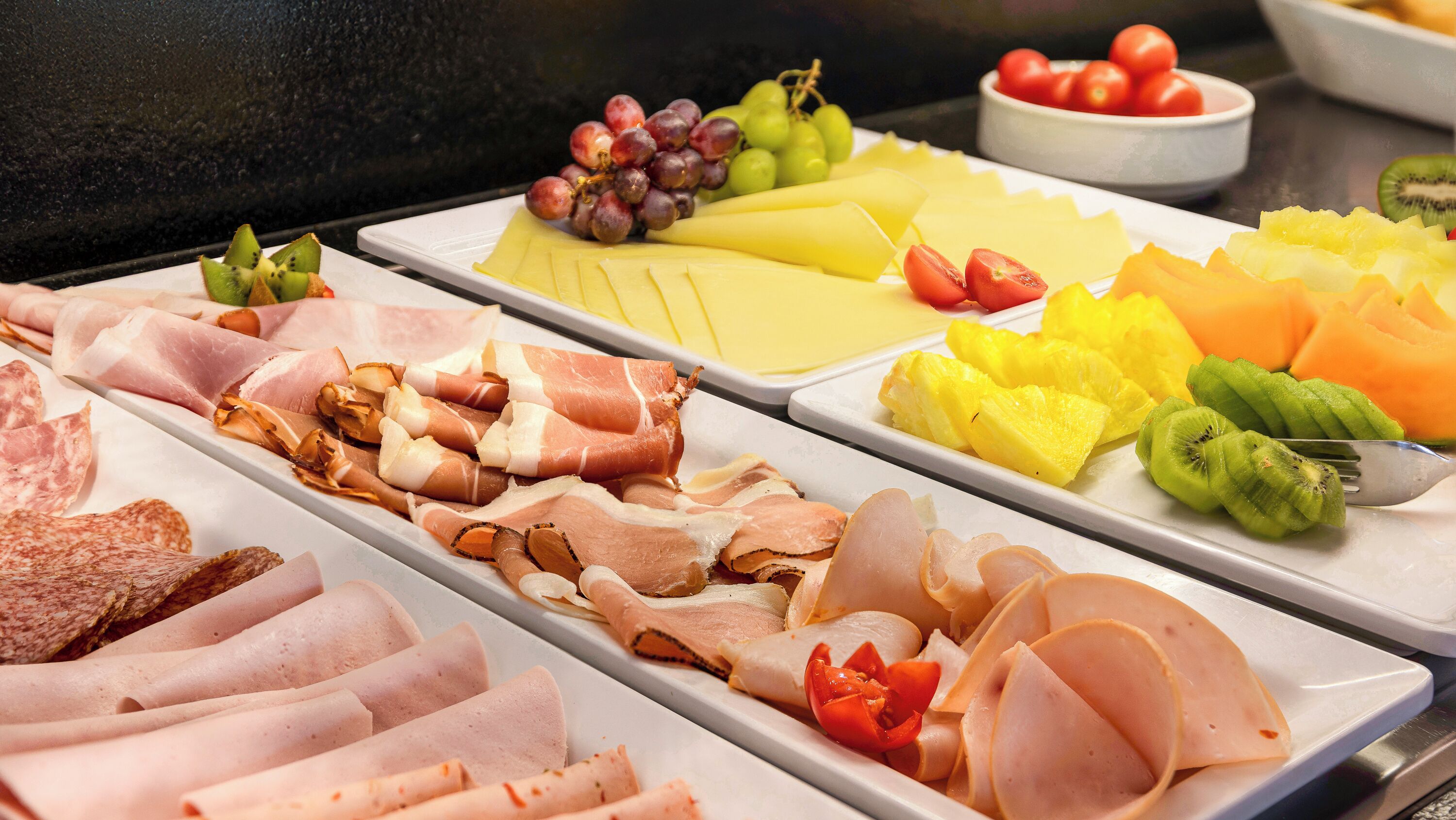 A buffet with various meats, cheeses, and fruits.