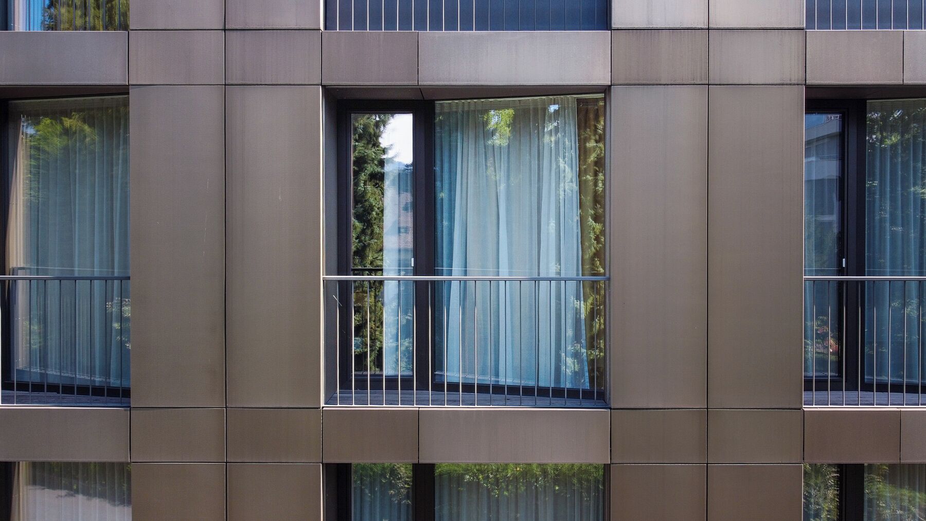 Fachada de edifício com várias janelas, cada uma com guarda-corpo de metal.