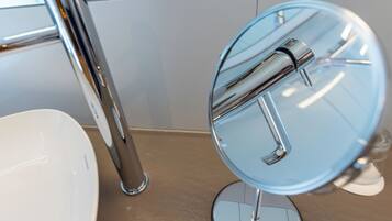 Un baño con un lavamanos blanco, una llave de cromo y un espejo redondo con base de cromo.