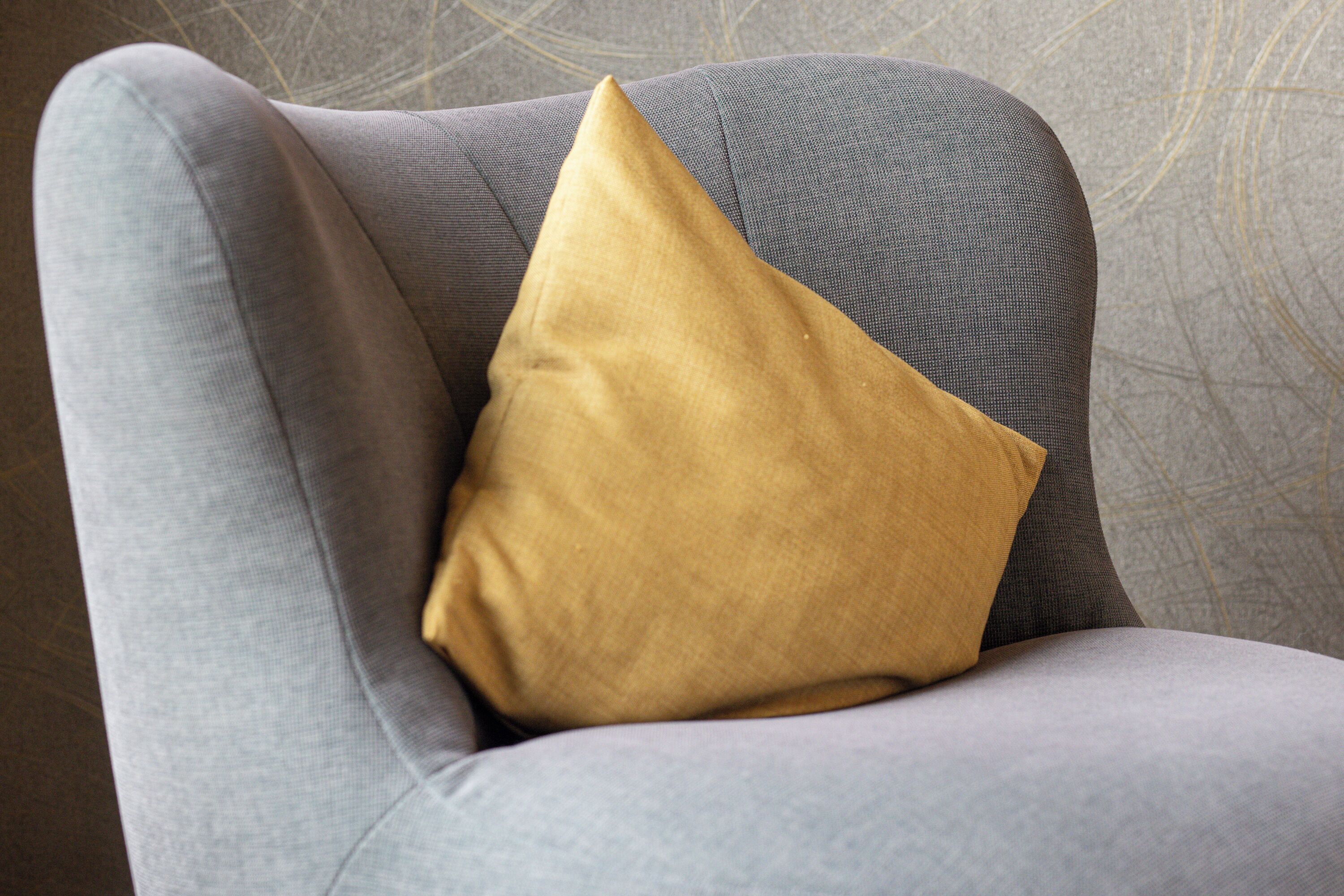 Un fauteuil à revêtement gris agrémenté d’un seul coussin de couleur moutarde.