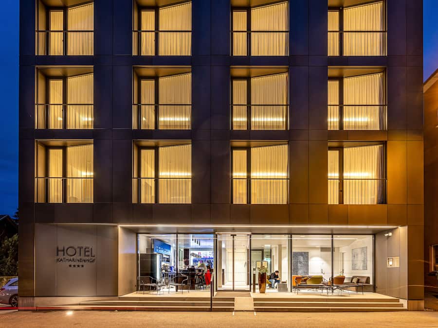 A modern hotel with a glass facade, multiple floors, and a visible restaurant area with seating.