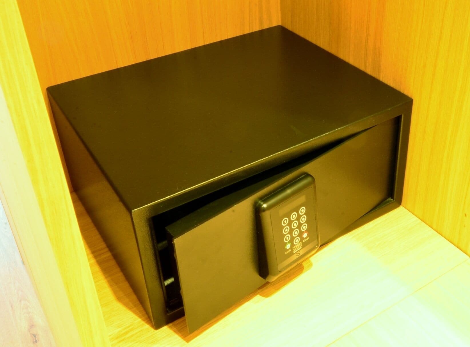 Una caja fuerte negra con teclado, ubicada frente a un fondo de madera.
