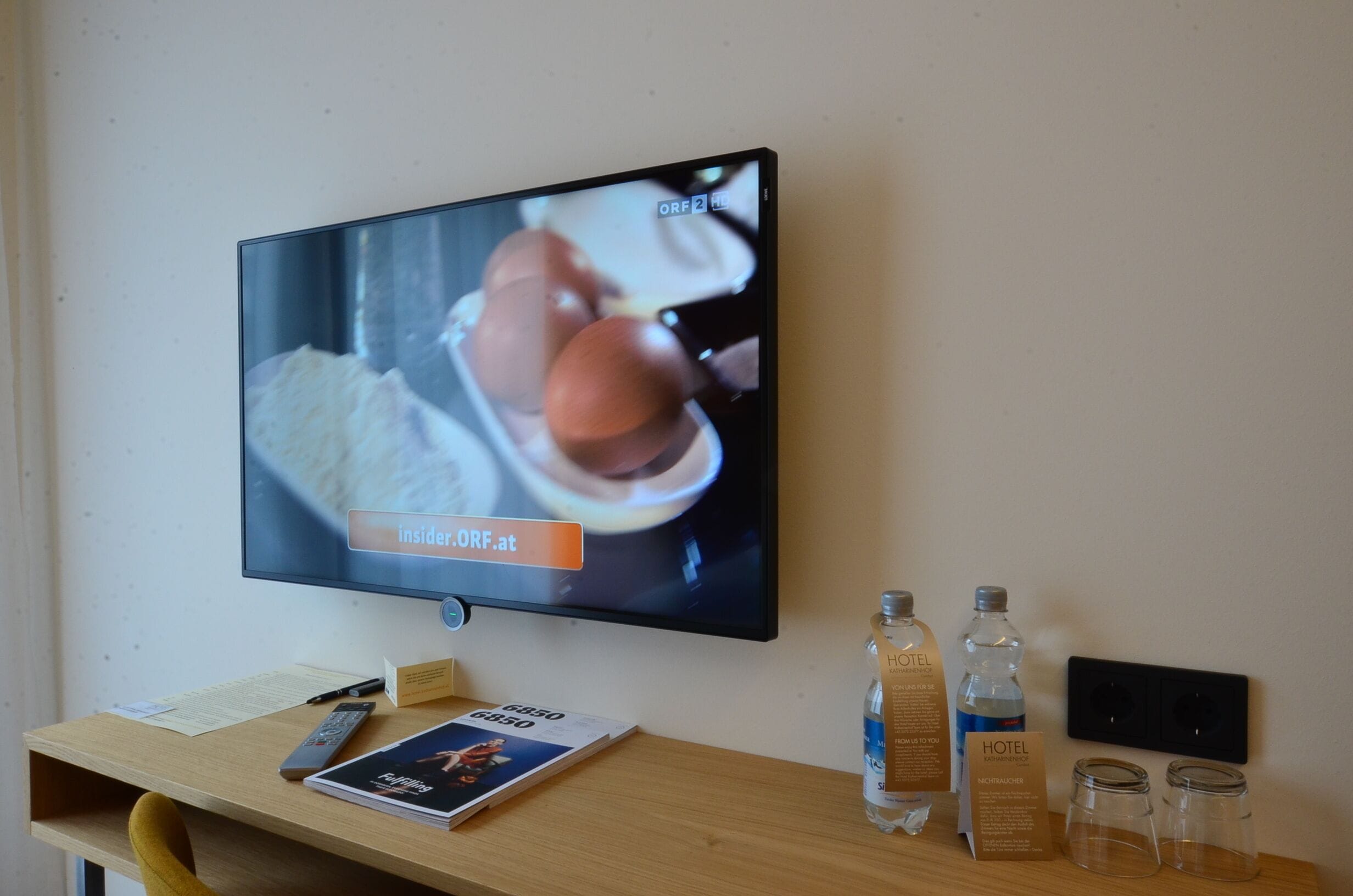 A television mounted on a wall displaying a scene with a person holding a drink.