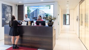 A reception desk with a large screen displaying a hotel image, a red carpet, and a potted plant.