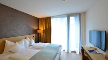 A hotel room with a large bed, a desk with a TV, and a window with curtains.