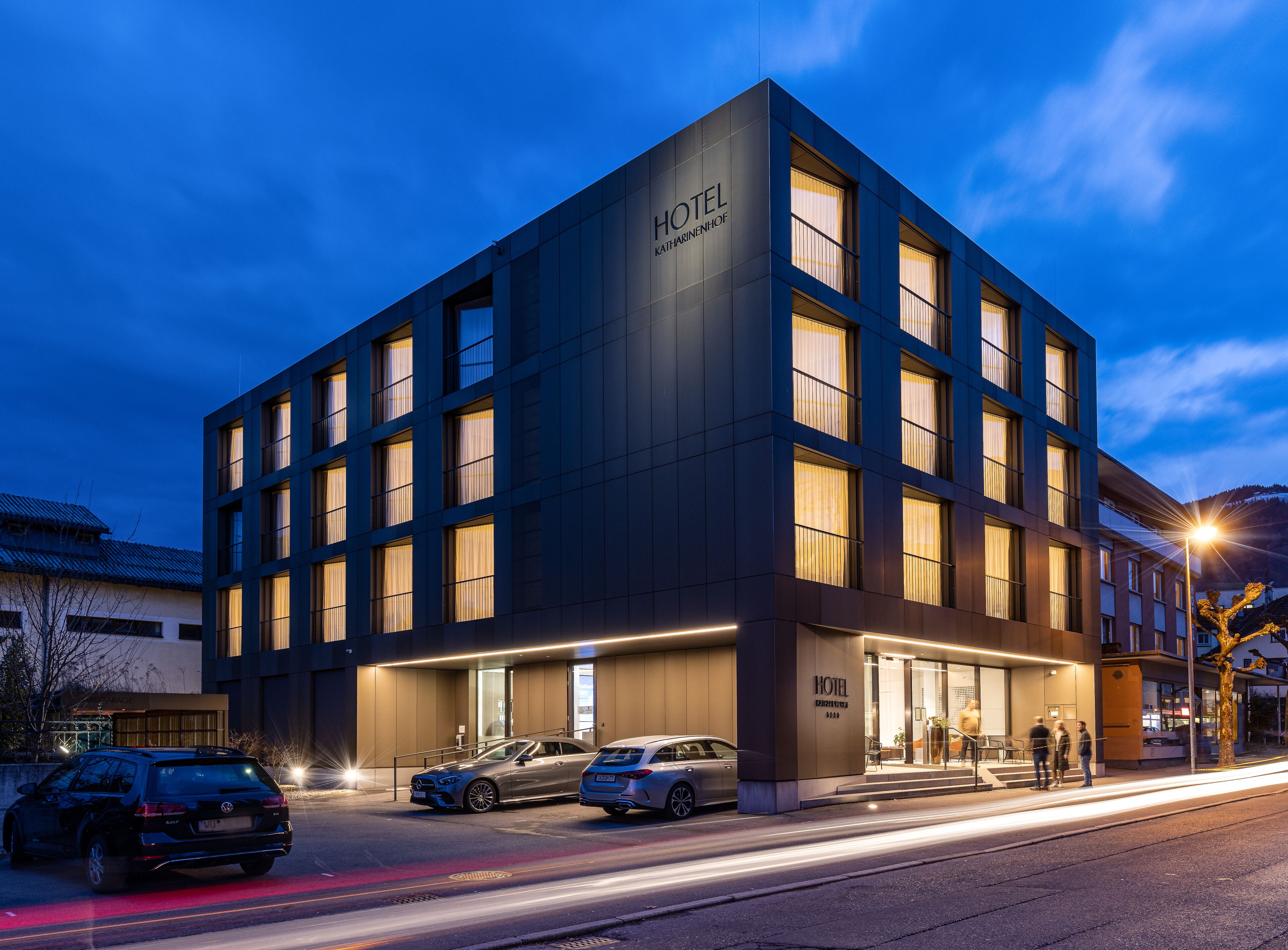 A modern hotel building with a prominent "HOTEL" sign, multiple windows, and a well-lit entrance.