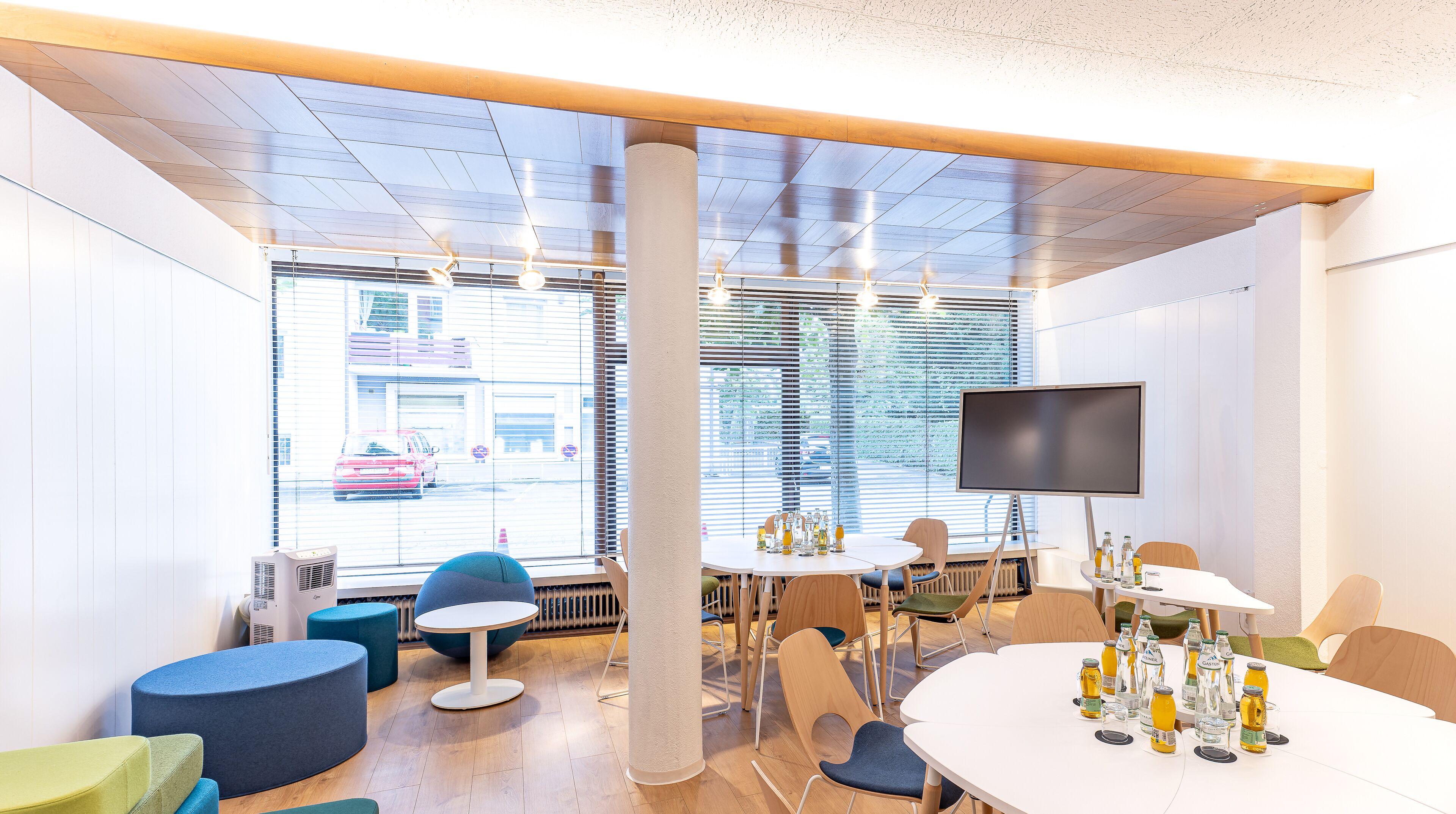 A modern meeting room with a large window, a flat-screen TV, and various seating arrangements.