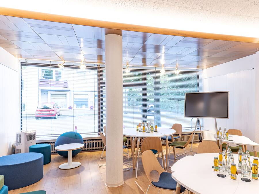 A modern meeting room with a large window, a flat-screen TV, and various seating arrangements.
