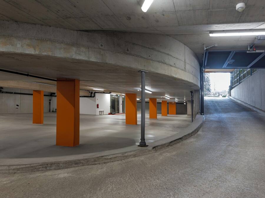 An indoor parking garage with concrete pillars, a curved ceiling, and fluorescent lighting.