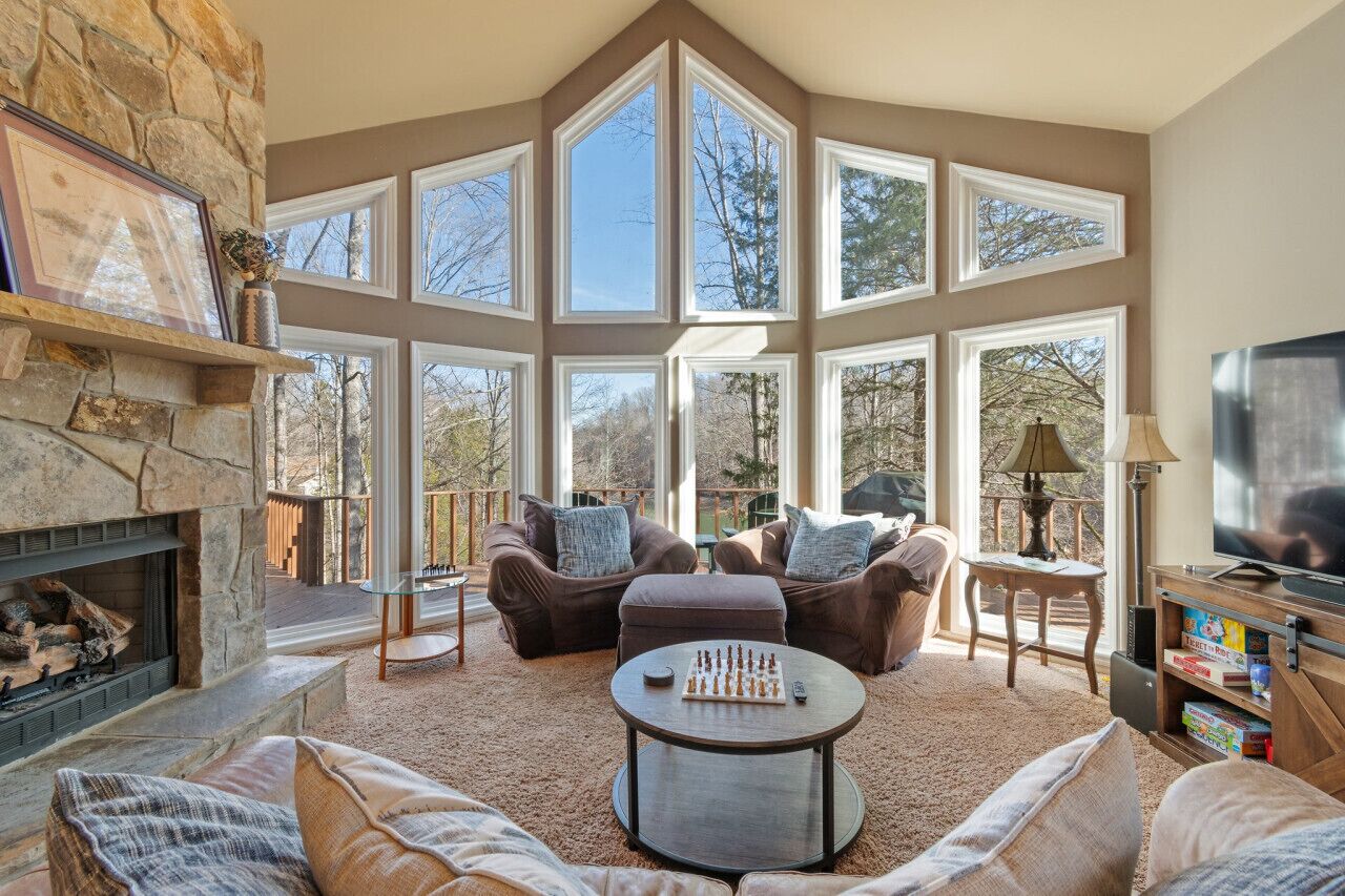 A spacious living room with a stone fireplace, large windows, comfortable seating, and a television.