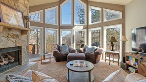 A spacious living room with a stone fireplace, large windows, comfortable seating, and a television. - Lakeside Haven w/Dock/Slip, Fire Pit, Game Room, Kayaks, (Winchester)