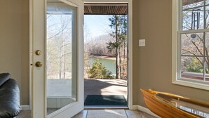 A room with a door leading to a scenic outdoor view of a lake and trees. - Lakeside Haven w/Dock/Slip, Fire Pit, Game Room, Kayaks, (Winchester)