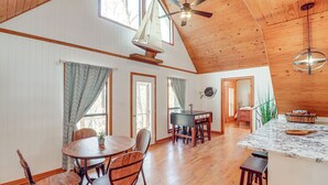 Un'ampia stanza con pavimento in legno, un'area pranzo con un tavolo rotondo e sedie, una cucina con isola in marmo e una ventola a soffitto.