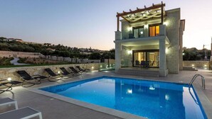 Une villa moderne dotée d’une piscine, de chaises longues et offrant une vue sur le paysage environnant.