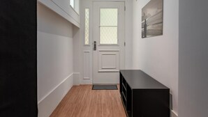 Un couloir avec un plancher en bois, une porte blanche, un banc noir et un tableau encadré accroché au mur.