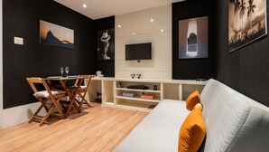Un salon moderne avec un canapé, une table à manger et des chaises, un téléviseur à écran plat et des œuvres d’art accrochées aux murs.