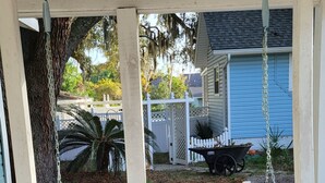 A white porch swing with striped cushions, a white fence, and a blue house in the background.