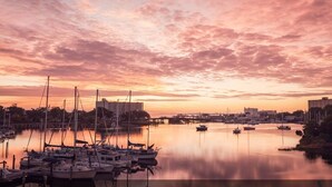 A marina with boats docked, calm water, and buildings in the background.