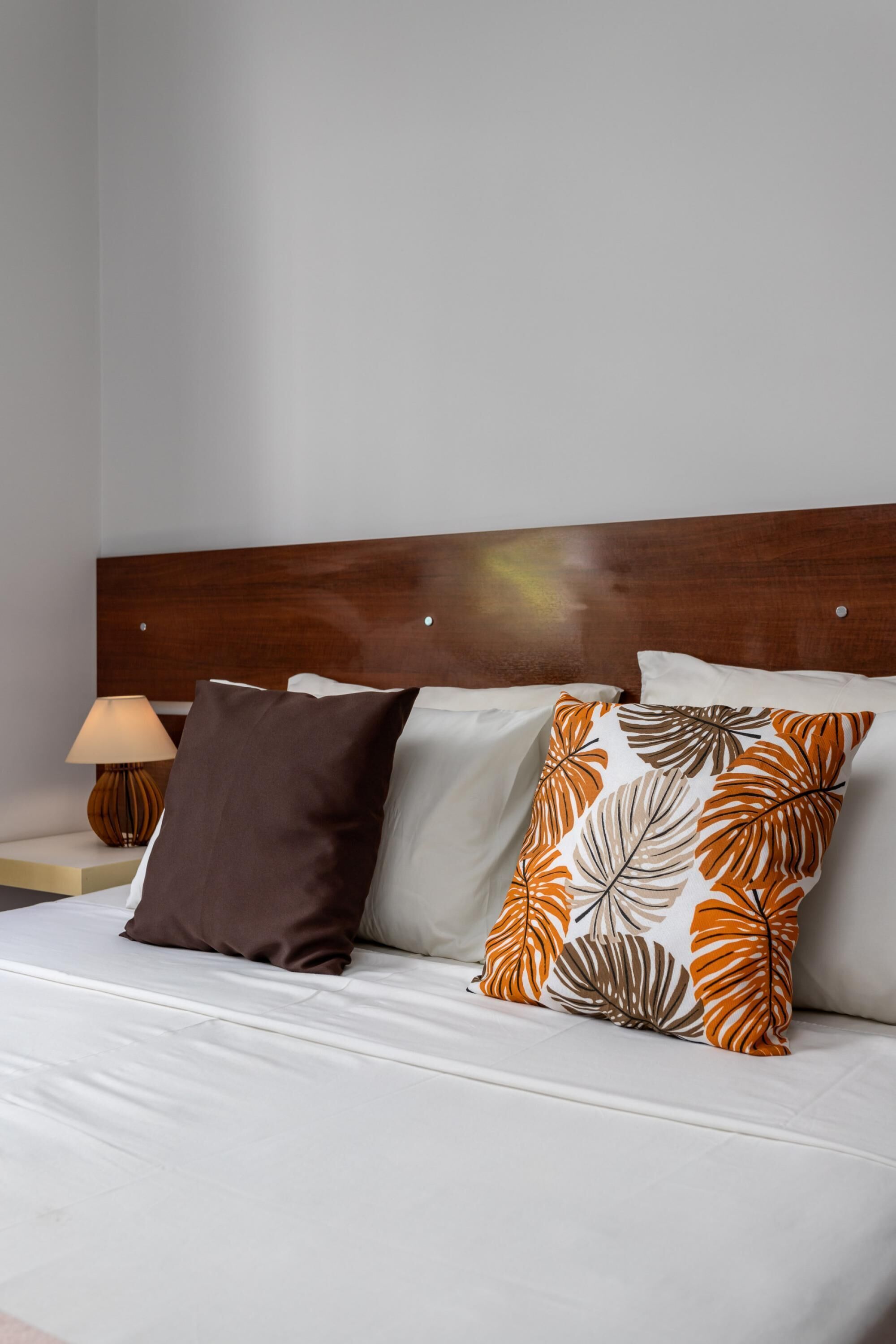 Una cama bien hecha con un cabecero de madera, ropa de cama blanca y dos almohadones decorativos con un diseño de hojas.
