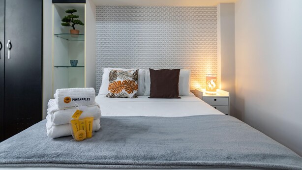 A neatly made bed with white linens, a brown pillow, and a decorative pillow with a leaf pattern. There are towels and toiletries on the bed, and a small plant on a shelf to the left. - Pleasant in Copa Ideal for Friends Sc602 (Rio de Janeiro)