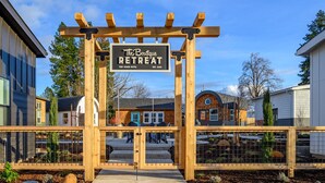 A wooden pergola entrance to The Boutique Retreat at Tiny House Hotel, with a clear view of the surrounding buildings and a well-maintained garden area.