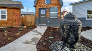 A modern house with a wooden facade, a grey door, and a large Buddha statue in the front yard.