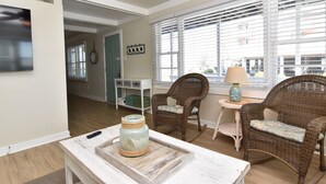 Una sala de estar acogedora con sillones de mimbre, una mesita con una lámpara y un televisor en la pared.