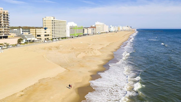 Una playa con una extensa franja de arena, algunas personas caminando y edificios al fondo.