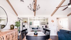Un coin repas avec une table en bois, des chaises noires et un lustre. Un canapé bleu est visible à l’arrière-plan.