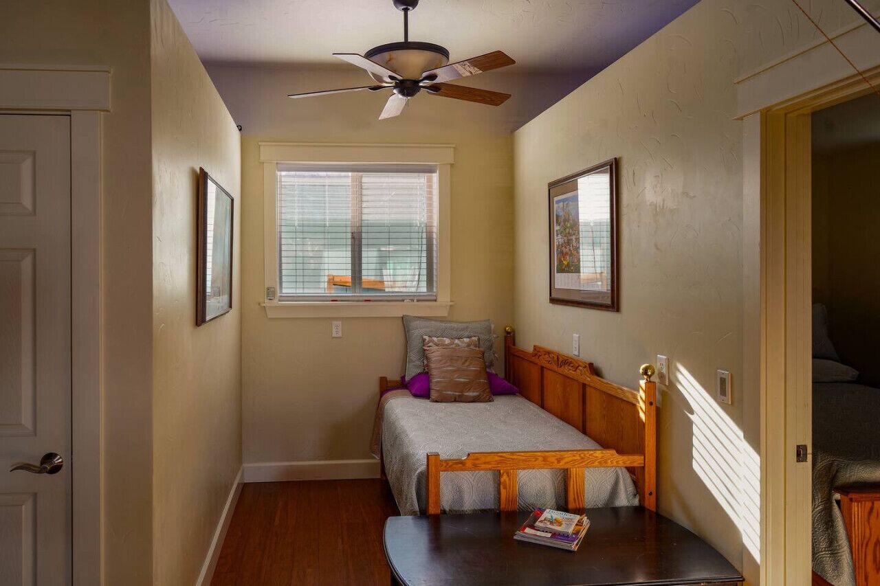 A bedroom with a single bed, a ceiling fan, a window with blinds, and a door.