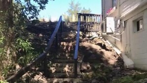 A set of stone steps leading up to a wooden structure with a blue railing. A black tire is visible on the ground.