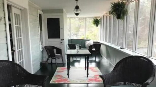 A covered porch with wicker chairs, a table, and a bench.