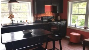 A kitchen with a central island, a sink, and a stove. There are two windows providing natural light and a view of greenery outside.