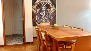 Un comedor con una mesa y sillas de madera, un colorido mural geométrico, y una puerta que da a otra habitación.