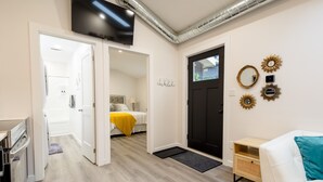 Une chambre d’hôtel moderne équipée d’un téléviseur à écran plat, d’un lit avec une couverture jaune, d’un canapé blanc et d’une petite table d’appoint en bois.