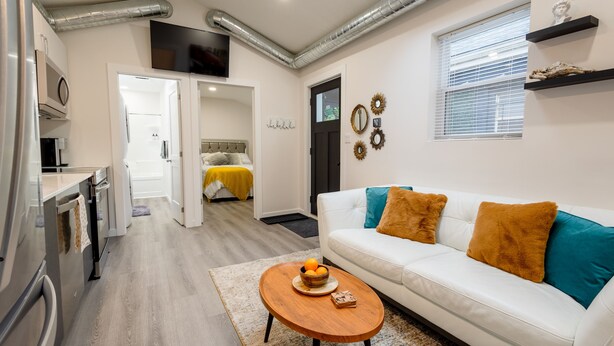 Un salon moderne avec un canapé blanc, une table basse en bois et un coin cuisine équipé d’un four à micro-ondes.