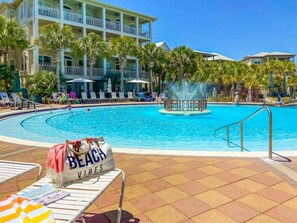 Zona de piscina con sillones, una fuente de agua y un edificio con balcones.