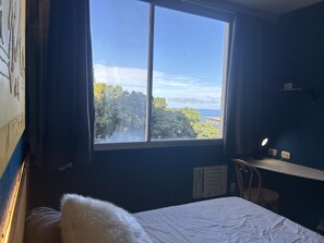 A bedroom with a large window, a bed, a desk, and a chair. - Estúdio Azul "Da cor do Mar" um lugar com tudo em cima para curtir a região. (Vidigal)