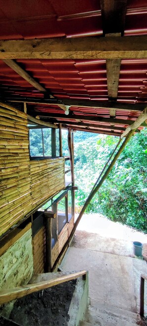 A rustic wooden structure with a red roof, bamboo walls, and a window overlooking a forested area. - Cabaña Tabachín - Su conexión con la naturaleza (Santa María Huatulco)