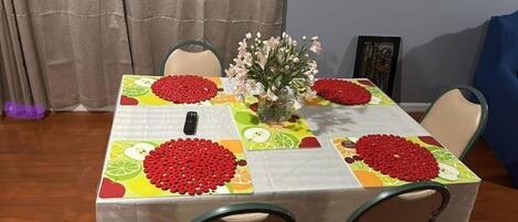 A dining table with a colorful tablecloth, a vase with flowers, and red fruit decorations.