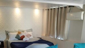 Una habitación de hotel moderna con una cama, dos sillones azules, una mesita redonda con dos tazas y una silla blanca.