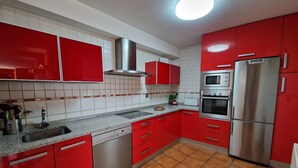 A kitchen with red cabinets, a stainless steel refrigerator, a built-in oven, and a dishwasher.
